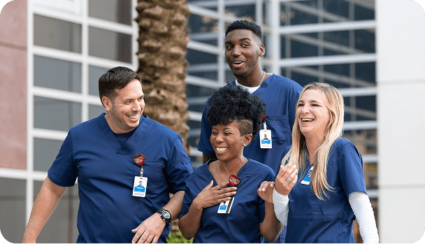 Four smiling and laughing healthcare professionals walking outside of an AdventHealth healthcare facility