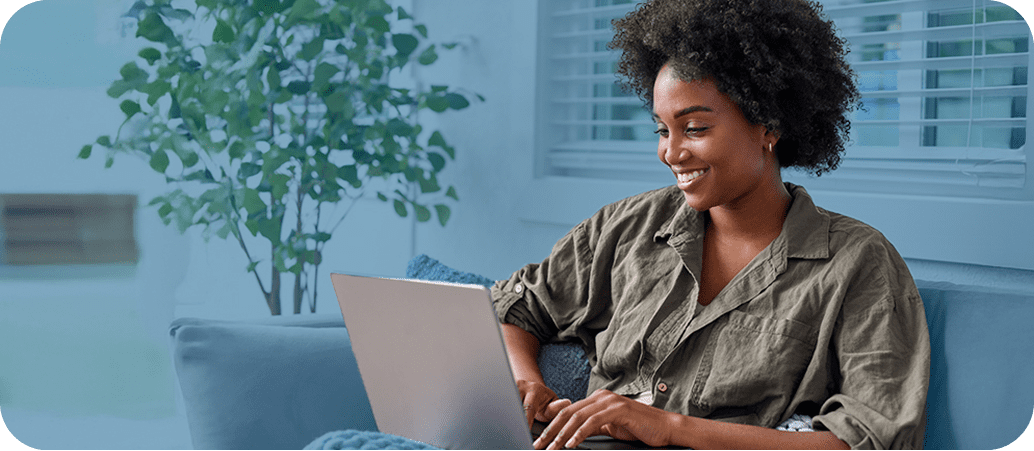 A smiling woman sitting on a couch in her living room and working on a laptop computer